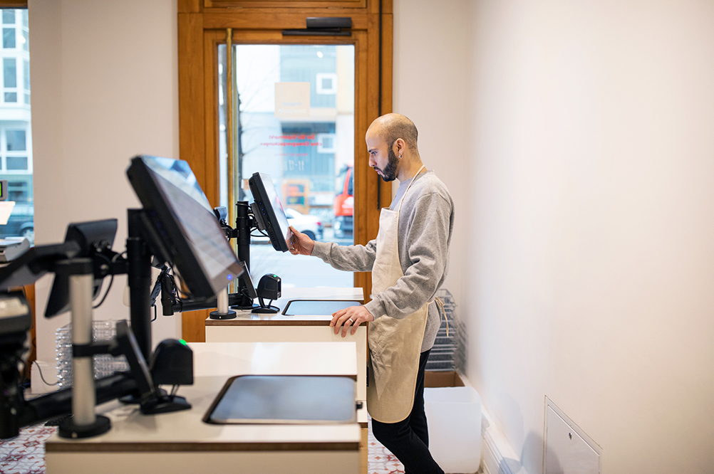 Man som står vid ett kassasystem i en butik, kassasystem som är anpassade för specifika verksamheter.